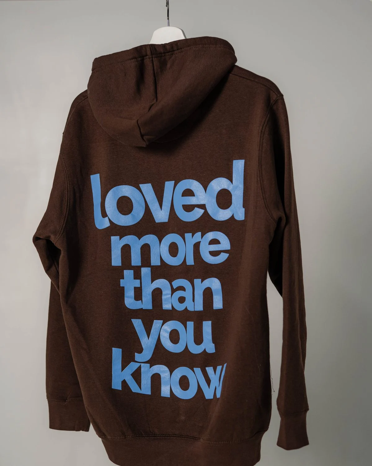 Espresso brown Loved hoodie, back: “loved more than you know” in light blue